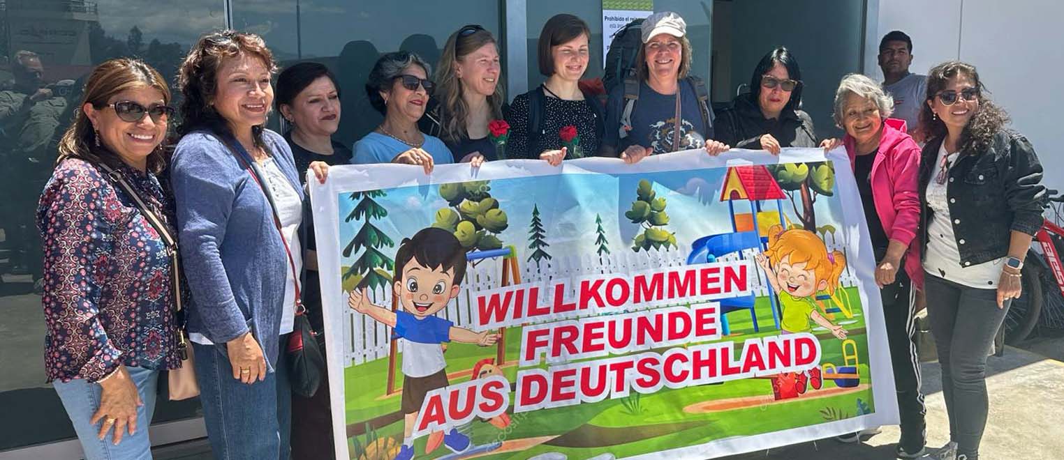 Viele Frauen stehen vor dem Eingang des Flughafens in Cajamarca und halten ein Schild hoch. Au dem Schild steht geschrieben: Willkommen Freunde aus Deutschland.